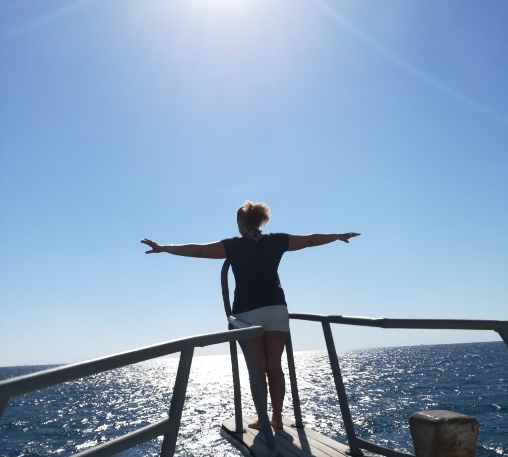 a women in the front of a ship arms strected out to the sides like embracing the world and her view on the sea in front of her