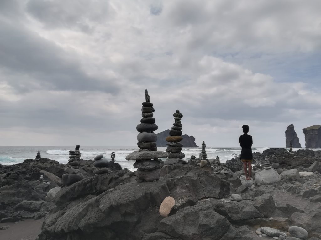 Einsamer Mensch steht neben Steinfiguren vor einem bewölkten Himmel und einem stürmischen Meer